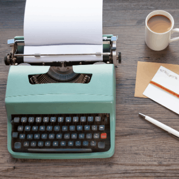 A typewriter on a table with coffee, a pen, and a note.