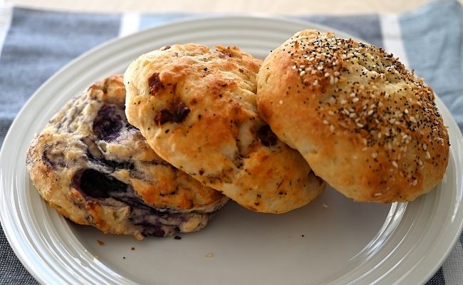 A blueberry bagel, sundried tomato basil bagle, and everything bagel stacked together.