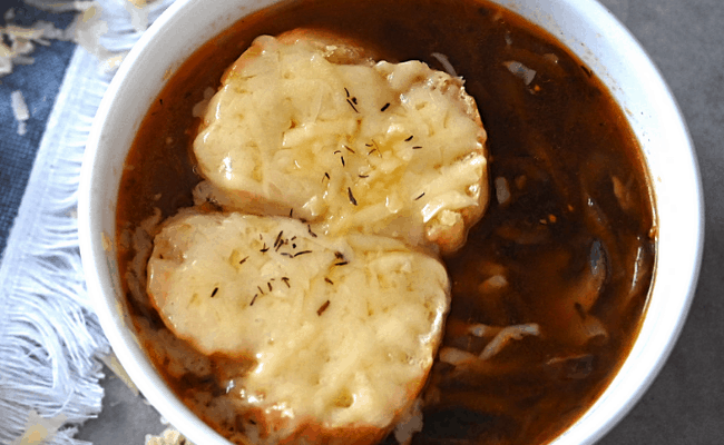 A bowl of vegetarian french onion soup topped with a baguette and cheese.