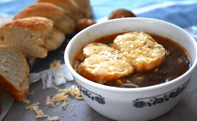 A bowl of vegetarian french onion soup with a baguette.