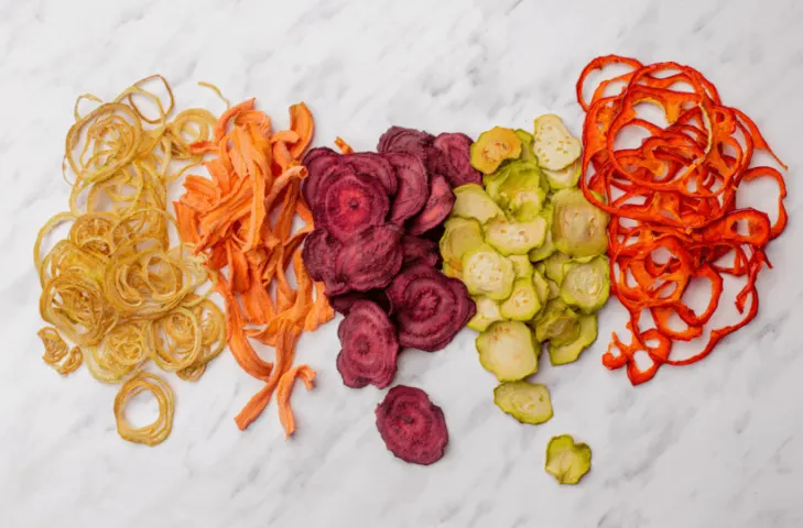 A line of dehydrated vegetables in order from left to right: onions, carrots, beets, cucumbers, red peppers.